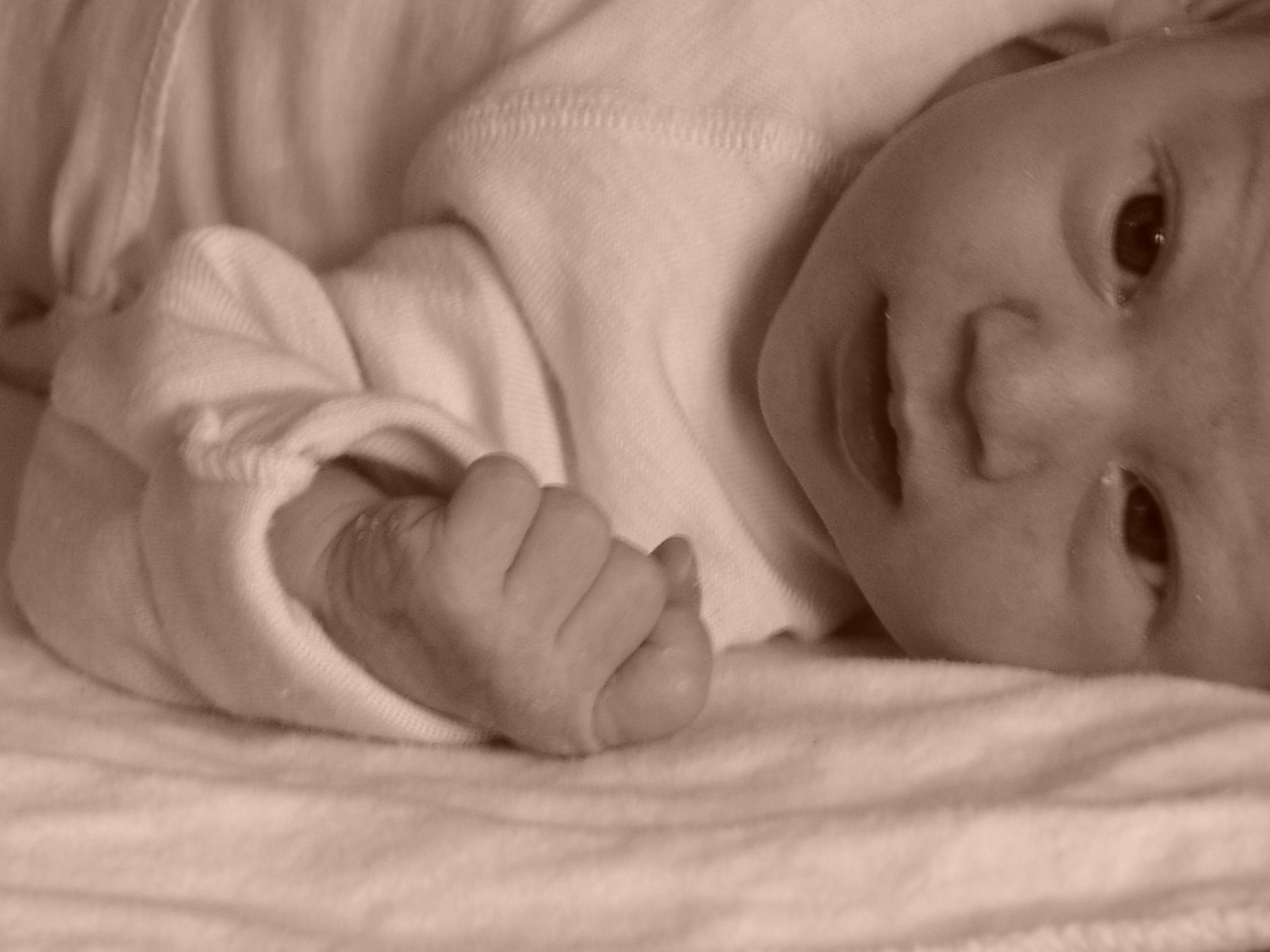 Louella bébé, poing fermé, joue au sol, regard qui suit la main — le réflexe de grasping